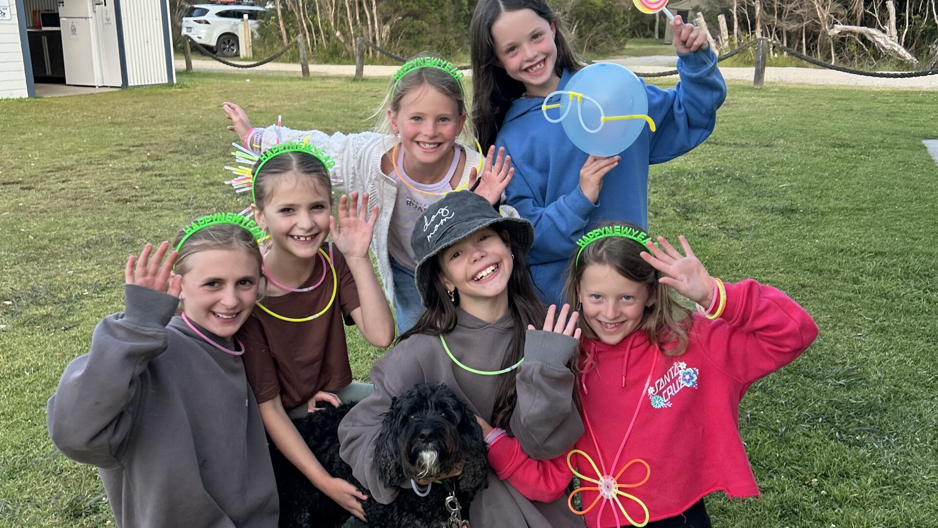 Kids posing for a picture with glow sticks and a dog on park grounds